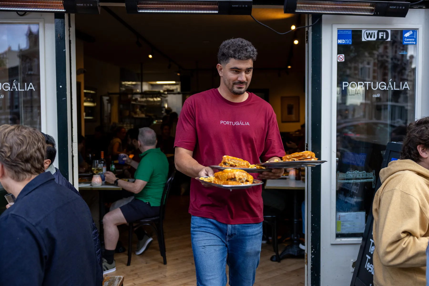 De bediening van Portugalia Churrasco in Rotterdam komt met borden door de deur, met gasten aan weerszijden